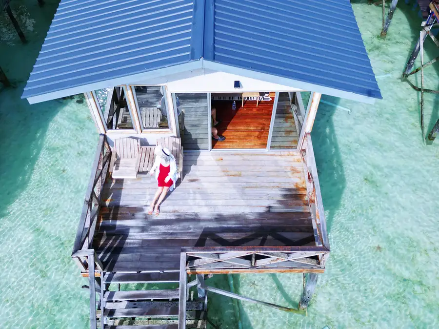 A sweeping sunset aerial view of timber overwater villas featuring high-pitched roofs and private balconies, embodying classic indigenous architecture at Fairyland Resort.