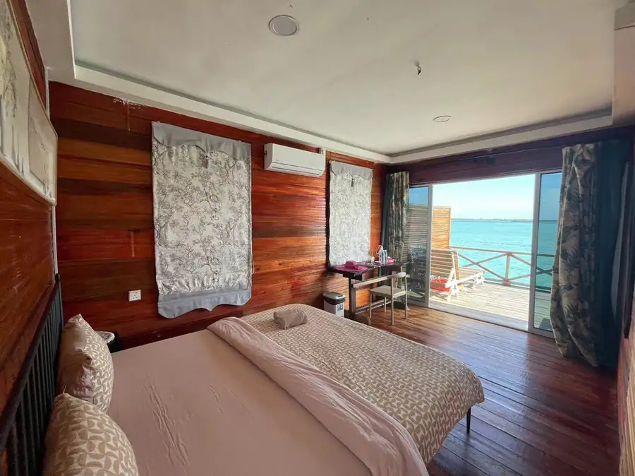 A bright bedroom at Fairyland Resort near Semporna detailing a bed facing panoramic glass doors opening onto the private balcony with seaviews, elegant hardwood floors, and aircon.