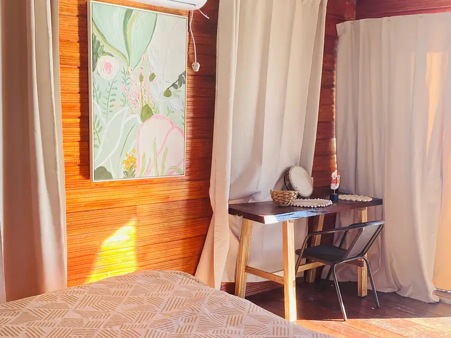 A bedroom workspace at Fairyland Resort near the Tun Sakaran Marine Park featuring a desk, floral artwork, traditional Sabahan style wood paneling with gleaming timber floors, and air conditioning.