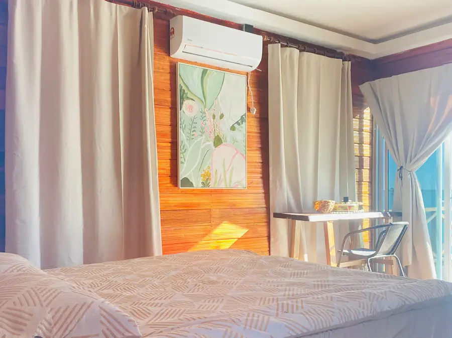 A warm bedroom at Fairyland Resort near Semporna showcasing a comfortable bed, vibrant floral wall art, a window desk, rustic timber floor with smooth wooden boards, and air con.