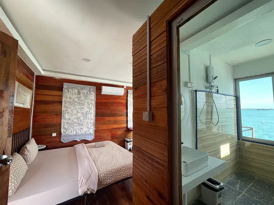 A relaxing bedroom at Fairyland Resort near Bum Bum Island, showcasing a large bed, connected bright en-suite, authentic wooden walls, glossy hardwood floors, and refreshing air con.