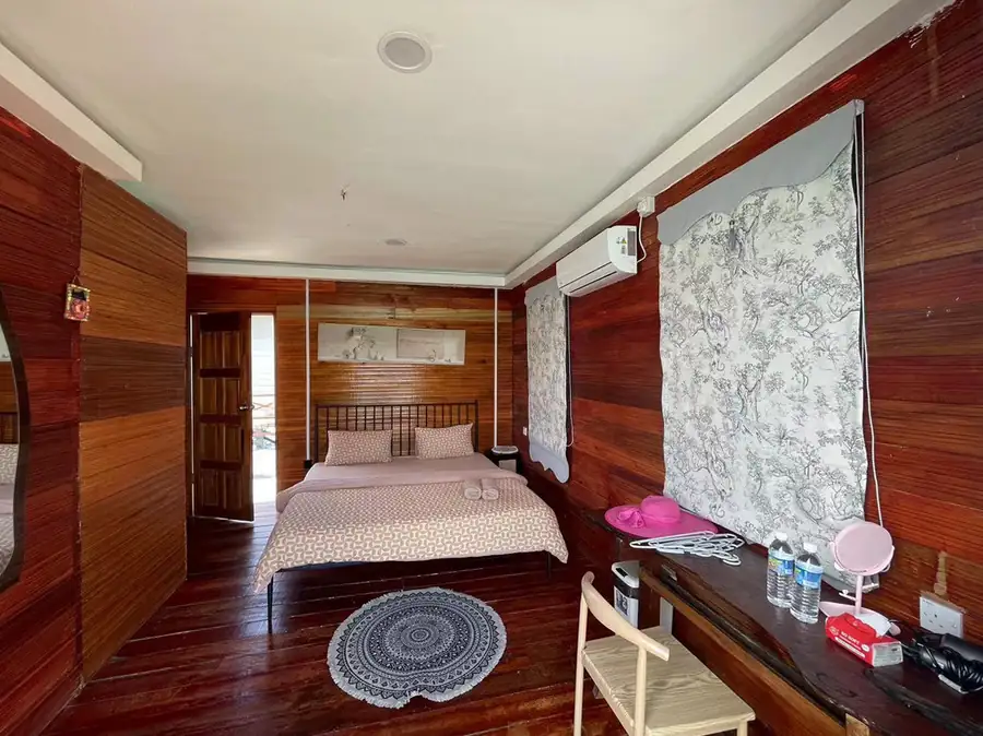 A cozy bedroom at Fairyland Resort near Pulau Bum Bum featuring a large bed, patterned curtains, an open wooden door, warm wooden plank walls with smooth timber floors, and AC.