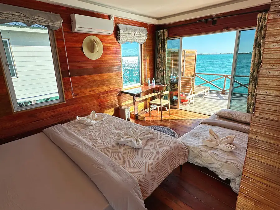 A simple bedroom at Fairyland Resort near Bohey Dulang highlighting a comfortable bed with crisp white linens and plush pillows, authentic hardwood floors, and air con.