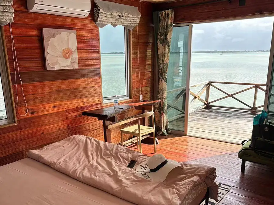 A rustic bedroom at Fairyland Resort in the Celebes Sea showing a cozy double bed with geometric patterned linens, wood paneling, beautiful polished teak wood floors, and air conditioning.