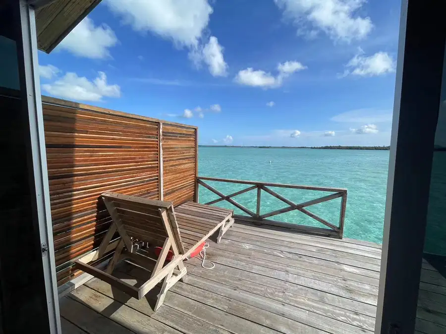 Private sunlit balcony with ocean views at Fairyland Resort. A serene over the water escape in Semporna featuring a wooden lounge chair and cool tropical breeze above crystal-clear waters.