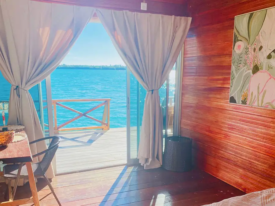 An inspiring workspace inside a room at Fairyland Resort on the Celebes Sea, offering floor to ceiling glass doors to a sunny balcony, traditional Sabahan style wood paneling, polished floors, and A/C.