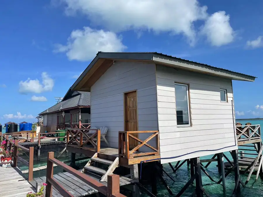 A traditional Sabah style overwater chalet featuring a distinctive pointed roof with ornate finials, dark timber siding, and a private plunge pool on the wooden deck at Fairyland Resort.