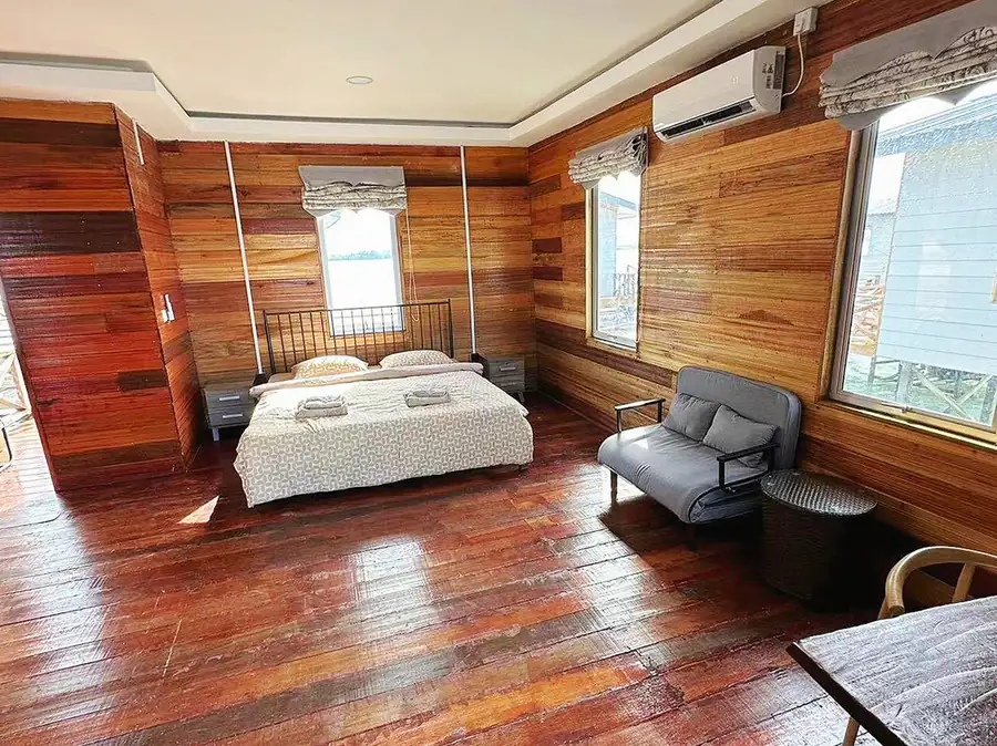 A serene bedroom at Fairyland Resort by Tun Sakaran, featuring a cozy bed, comfortable sofa, large sea-facing windows, handcrafted wooden slat walls, polished timber floors, and efficient A/C.