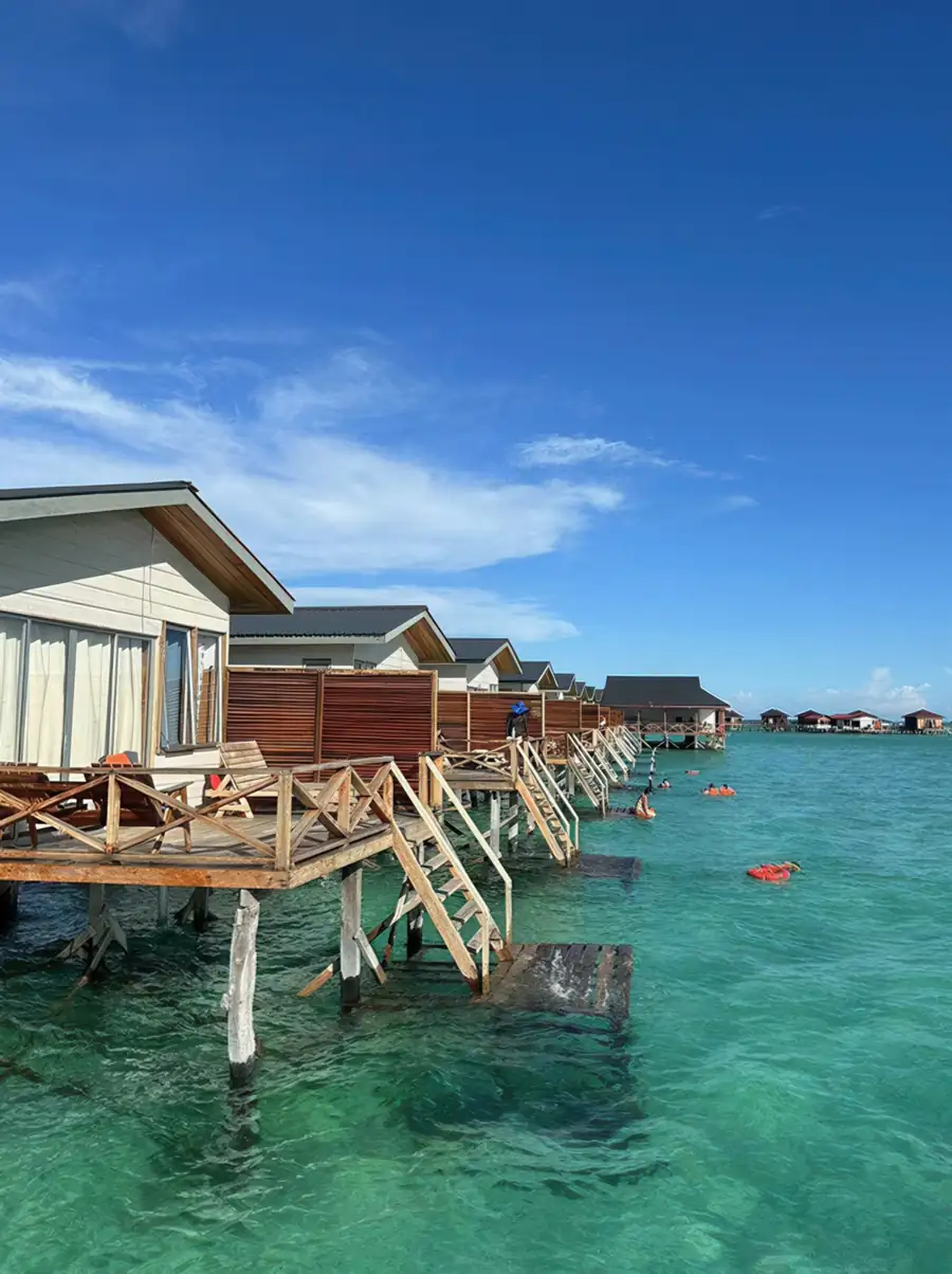 A local style wooden chalet featuring a high-pitched traditional roof, dark timber walls, and an overwater private deck equipped with a hammock net at Fairyland Resort.