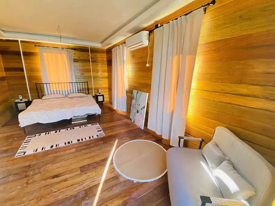 A glowing bedroom at Fairyland Resort in Semporna, offering a sunlit space with a plush bed, modern sofa, authentic wooden walls, glossy hardwood floors, and a modern air conditioning system.
