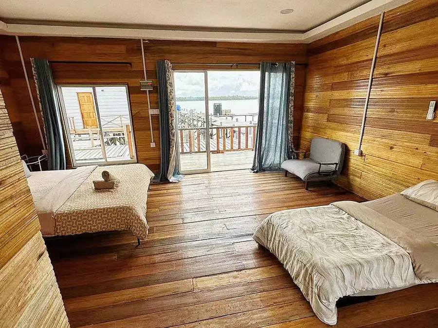 A bright family room at Fairyland Resort in the Tun Sakaran Marine Park featuring beds facing floor to ceiling glass doors, classic wooden planking with varnished timber flooring, and A/C.