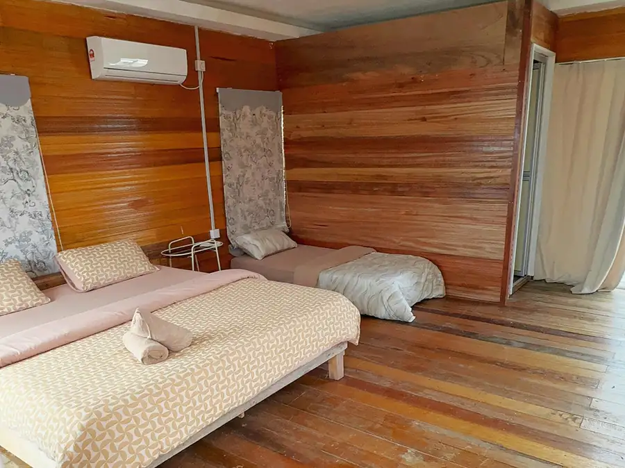 A spacious family bedroom at Fairyland Resort on the Celebes Sea featuring one large bed and a single bed, authentic timber cladding with smooth wooden boards, and air conditioning.