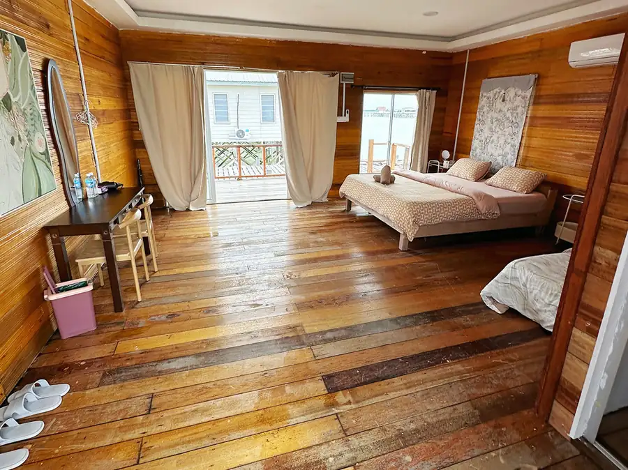 A spacious family bedroom at Fairyland Resort near Semporna, featuring beds facing glass doors opening onto the private balcony, warm wooden plank walls, varnished timber flooring, and AC.
