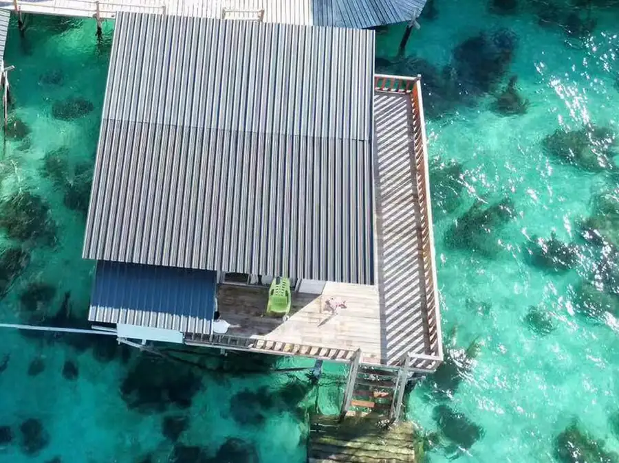 A direct overhead drone shot capturing timber overwater villas with pointed roofs and private balconies over clear waters, drawing on customary regional building techniques at Fairyland Resort.