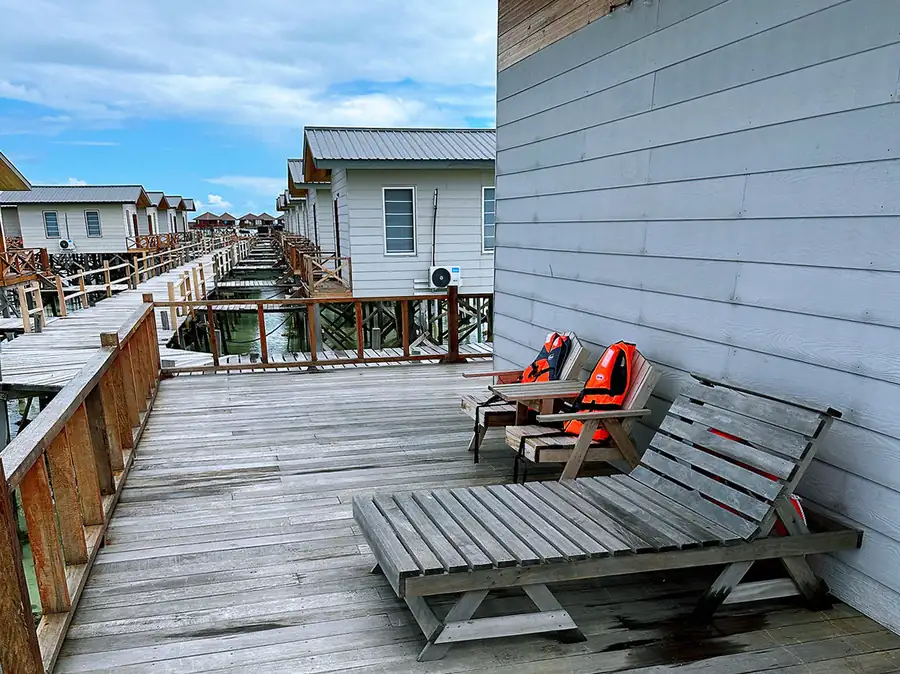 Private balcony overlooking the sea at Fairyland Resort, a unique Semporna water resort. The wooden deck features relaxing chairs and views of the neighboring overwater villas.