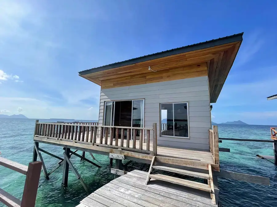 A traditional Sabah style overwater chalet at sunset featuring a high-pitched roof with cultural finials and a private wooden deck with a plunge pool at Fairyland Resort.