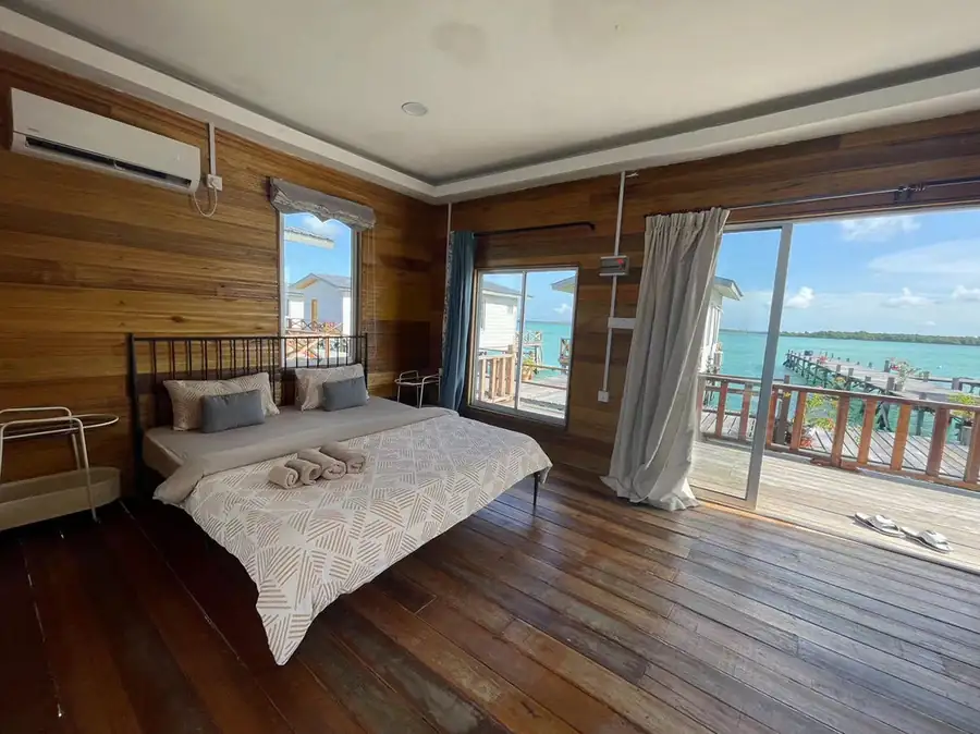 A stunning bedroom at Fairyland Resort on the Celebes Sea, showcasing a bed facing sliding glass doors to a breezy balcony, rustic timber walls, smooth wooden boards, and refreshing air con.